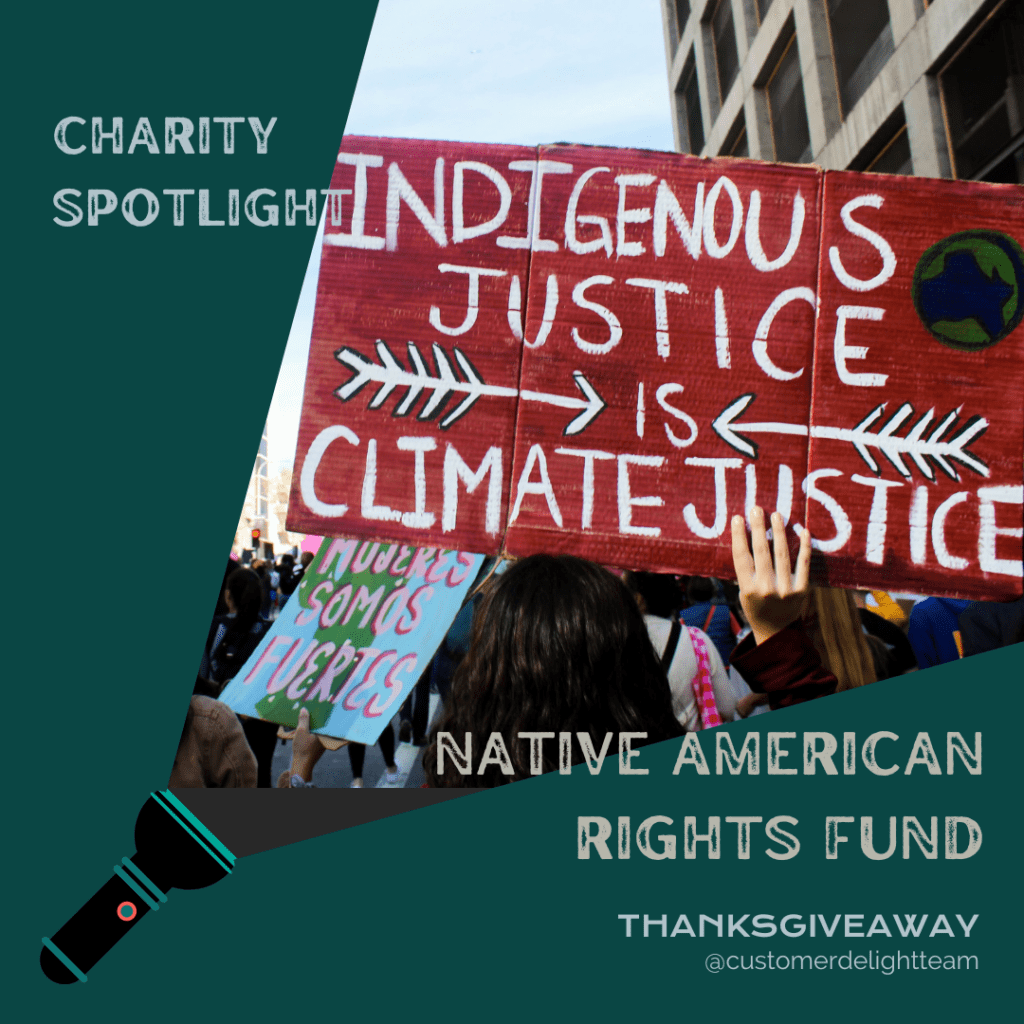 Photo of a protest sign that says "Indigenouse Justice Is Climate Justice" being held above a crowd and this photo is visible in the beam of light coming from a flashlight. The words "Charity Spotlight: Native American Rights Fund" surround the beam of light on a dark green background.