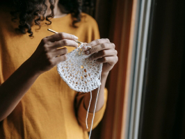 close up photo of a woman's hands holding a crochet needle and yarn, in the process of crocheting a round item. The photo represents customers using the things they buy as part of the customer experience.