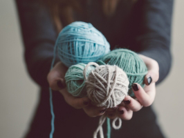 close up photo of a woman's hands holding 4 balls of yarn. The photo represents happy customers getting their hands on the things they buy - product delivery.
